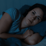Frau liegt wach im Bett und schaut zur Seite – Symbolbild für Schlaflosigkeit