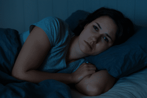 Frau liegt wach im Bett und schaut zur Seite – Symbolbild für Schlaflosigkeit