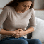 Frau hält ihre Hände auf den Bauch – Symbolbild für Verdauungsprobleme und Blähungen